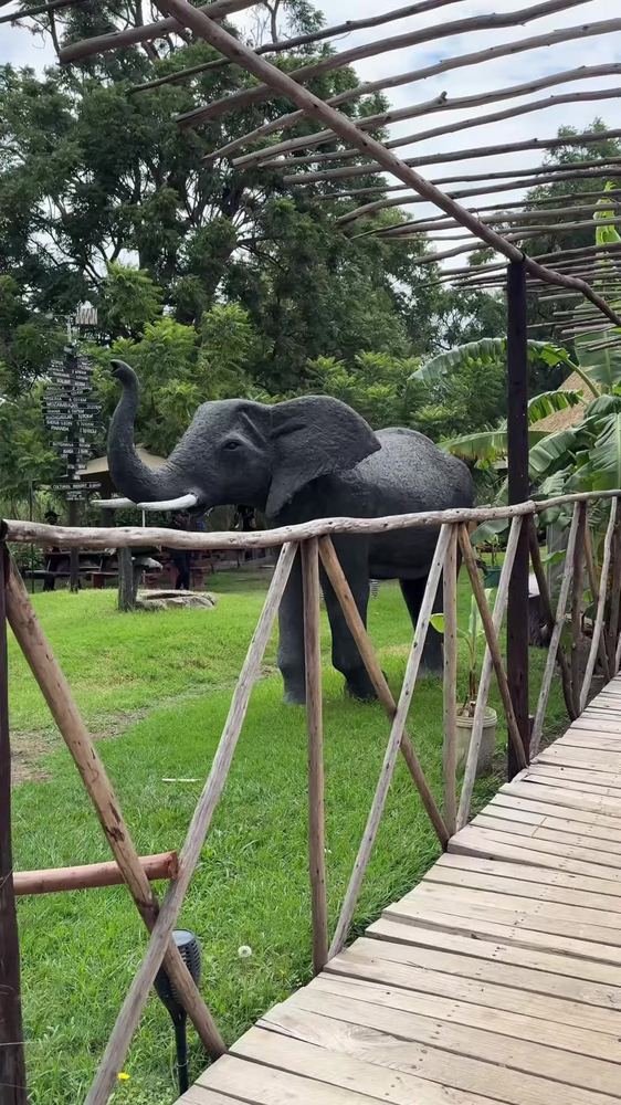 A life-size elephant sculpture beside a raised wooden walkway, with a signpost showing distances to African destinations