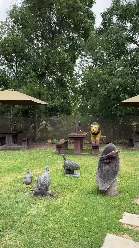 A lion sculpture and guinea fowl sculptures on the lawn among picnic tables