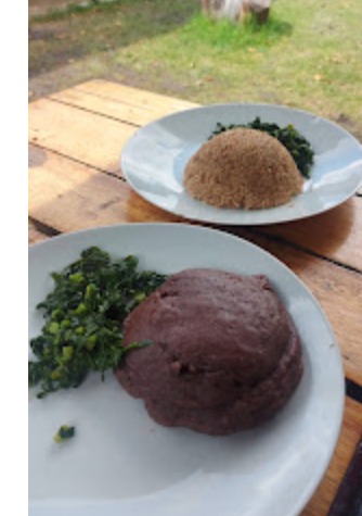 Sadza and covo served on a white plate at an outdoor wooden table